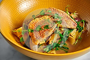 Pappardelle pasta with fried red mullet, barbule and microgrine in a yellow bright plate on a marble white background