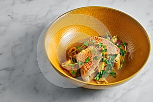 Pappardelle pasta with fried red mullet, barbule and microgrine in a yellow bright plate on a marble white background