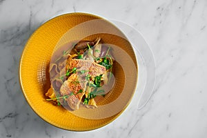 Pappardelle pasta with fried red mullet, barbule and microgrine in a yellow bright plate on a marble white background photo