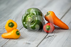 Paprika mix, sweet mini red, yellow and orange peppers and green pepper on a wooden background