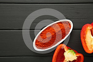 Paprika powder in plate with fresh red pepper on black background. Space for text