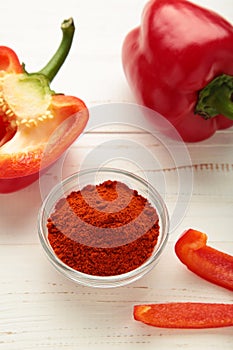Paprika powder in plate with fresh red pepper on white background. Vertical photo