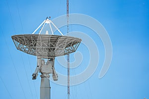 Parabolic antenna satellite dish located in front of telecommunication tower with a clear blue sky in the background