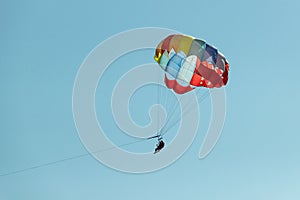 With a parachute for parasailing a couple flies through the air with blue sky in the background.