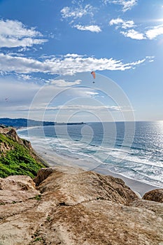 Parachuter and cloudy blue sky over ocean boredered by mountain in San Diego CA