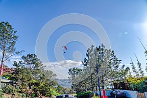 Parachuter flying over road homes and trees in San Diego California neighborhood