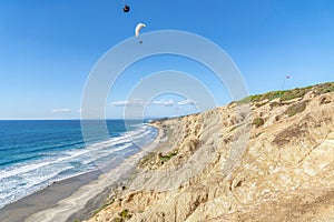 Parachuters over San Diego California landscape of blue ocean and rocky mountain
