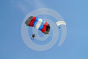 Parachuters, skydivers jumping and skydiving in parachutes of black red blue white colours on parachuting cup, extreme sport