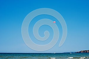 Parachuting over a sea, towing by a boat. Paragliding in the clear sky above the sea. Riding on a parachute behind a boat.