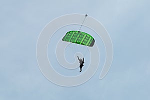 Parachutist with Green Parachute against Clear Blue Sky