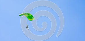 A parachutist with a light green parachute canopy against a background of blue sky and white clouds. Skydiving