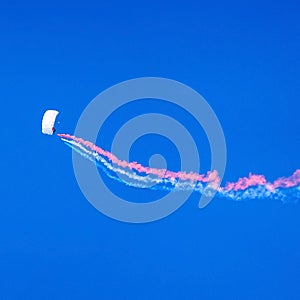 Parachutist seen against a deep blue sky trailing multicolor smoke