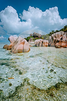 Paradise tropical beach Anse Source d`Argent with shallow blue lagoon, granite boulders and white clouds above. La Digue