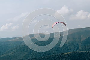 Paraglide silhouette flying over Carpathian peaks and clouds.