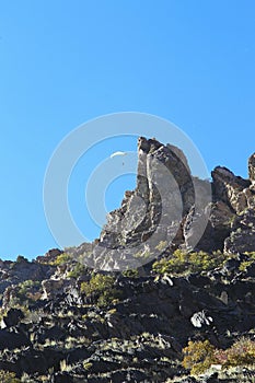 Paraglider in blue sky flying over rocky cliffs in autumn