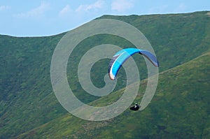 Paraglider flies over a mountain valley on a sunny summer day. Paragliding in the Carpathians in the summer.