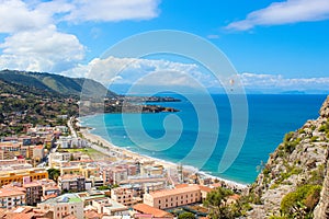 Paraglider flying above the amazing landscape of coastal city Cefalu in beautiful Sicily. Paragliding is a popular extreme sport.