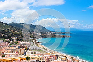 Paraglider flying above the beautiful seascape by city Cefalu in Sicily, Italy. Paragliding is a popular adventure sport.