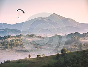 Paraglider flying above the misty carpathian hills