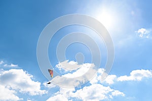 Paraglider flying against the blue sky with white clouds.