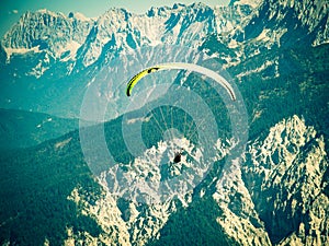 Paraglider flying over high and rugged range of Alps mountains