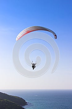 Paraglider flying over lush green mountains from view point on Koh Larn island in Pattaya, Chonburi Thailand