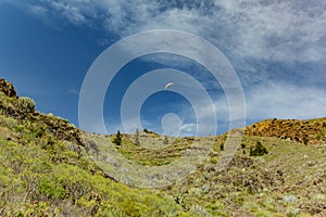 Paraglider flying over the mountains peaks against the bright blue sky. Sunny day. Clear blue sky and some clouds above the
