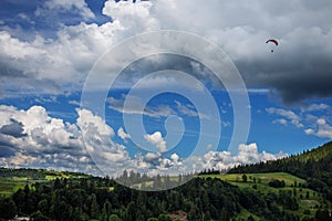 Paraglider flying over mountains during summer day