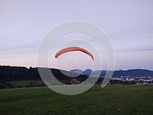 Paraglider flying on the parachute during sunset on the meadow.