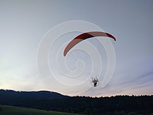 Paraglider flying on the parachute during sunset on the meadow.