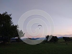 Paraglider flying on the parachute during sunset on the meadow.