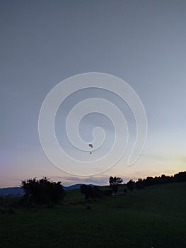 Paraglider flying on the parachute during sunset on the meadow.