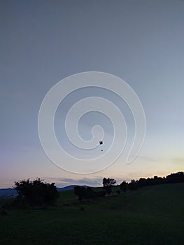 Paraglider flying on the parachute during sunset on the meadow.