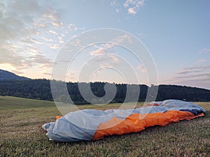 Paraglider flying on the parachute during sunset on the meadow.