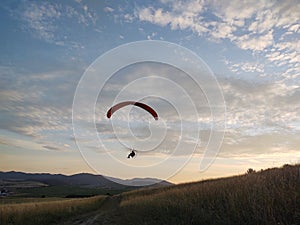 Paraglider flying on the parachute during sunset on the meadow.