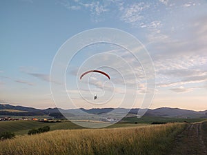 Paraglider flying on the parachute during sunset on the meadow.