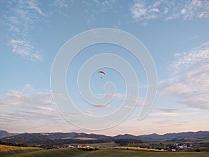 Paraglider flying on the parachute during sunset on the meadow.