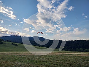 Paraglider flying on the parachute during sunset on the meadow.