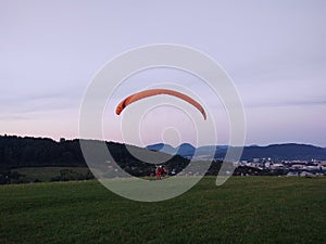 Paraglider flying on the parachute during sunset on the meadow.