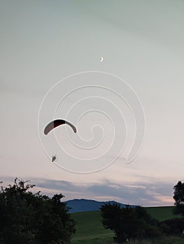 Paraglider flying on the parachute during sunset on the meadow.