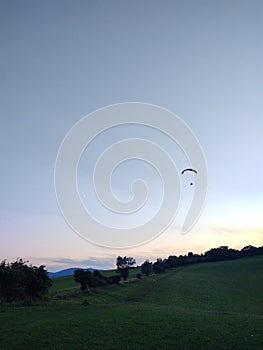 Paraglider flying on the parachute during sunset on the meadow.