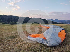 Paraglider flying on the parachute during sunset on the meadow.