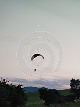 Paraglider flying on the parachute during sunset on the meadow.