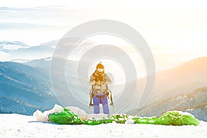 Paraglider in helmet with sun behind him preparing to get launched from snowy slope