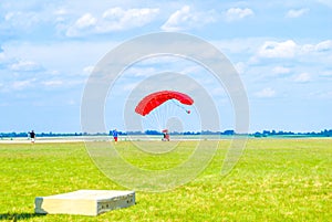 Paraglider landing on summer green fields by blue sky