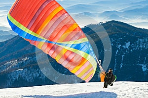 Paraglider launching into air from the very top of a snowy mountain slope