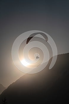 Paraglider over the silhouette of a wooded mountain ridge with the sun backlit