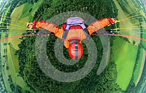 Paraglider pilot with orange clothes and red helmet flying in 500 ft above a forest