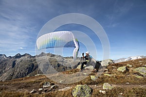 Paraglider pilot sits on a rock and balances his paraglider above his head near Lake Grimsel in the Swiss Alps