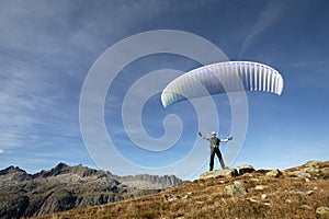 Paraglider pilot stands on a rock and balances his paraglider above his head near Lake Grimsel in the Swiss Alps